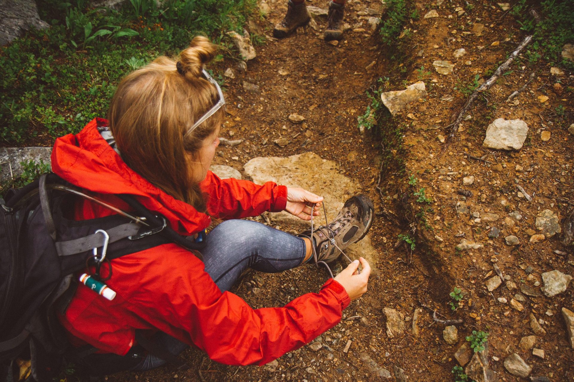 woman sitting on ground fixing her hiking shoes
