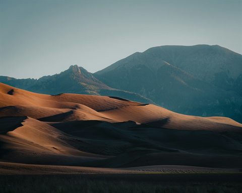 Broad sand dunes backed by a rugged mountain range