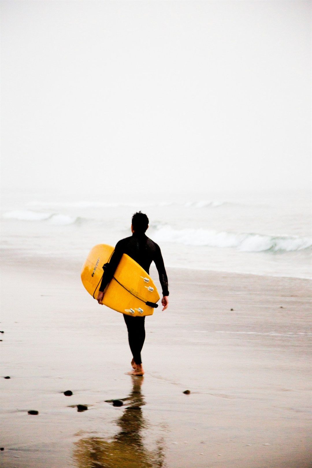 Surfer walking toward the Pacific Ocean at Carlsbad beach
