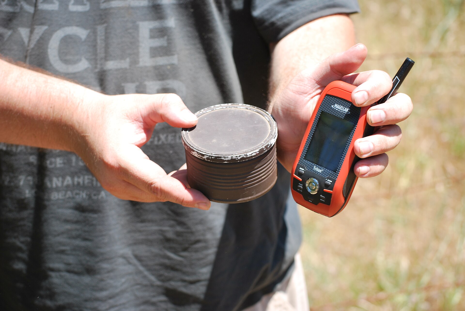 A handheld GPS receiver beside a small geocache