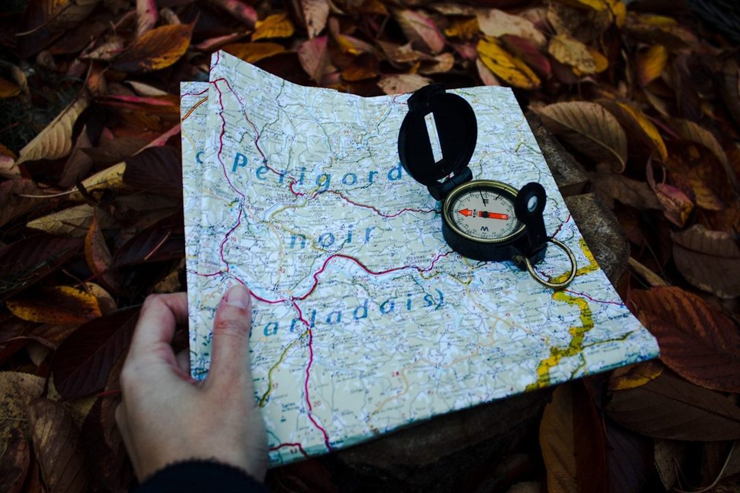 Hand holding a trail map and compass among autumn leaves