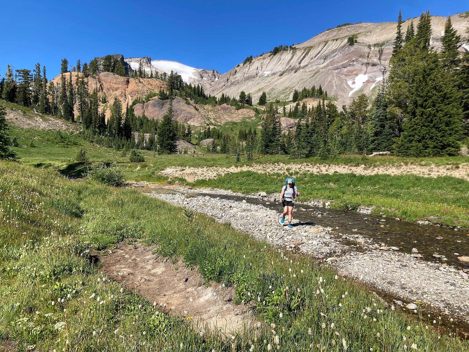A backpacker approaching a shallow stream crossing in mountain terrain