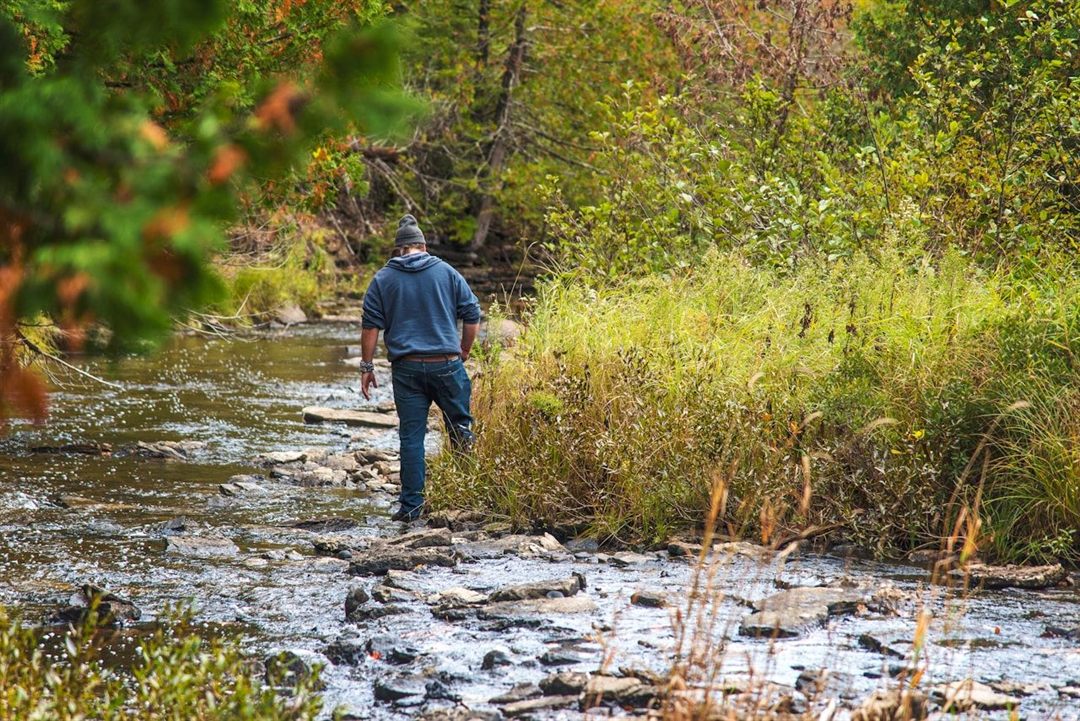Hiker carefully making his way across a shallow rocky stream