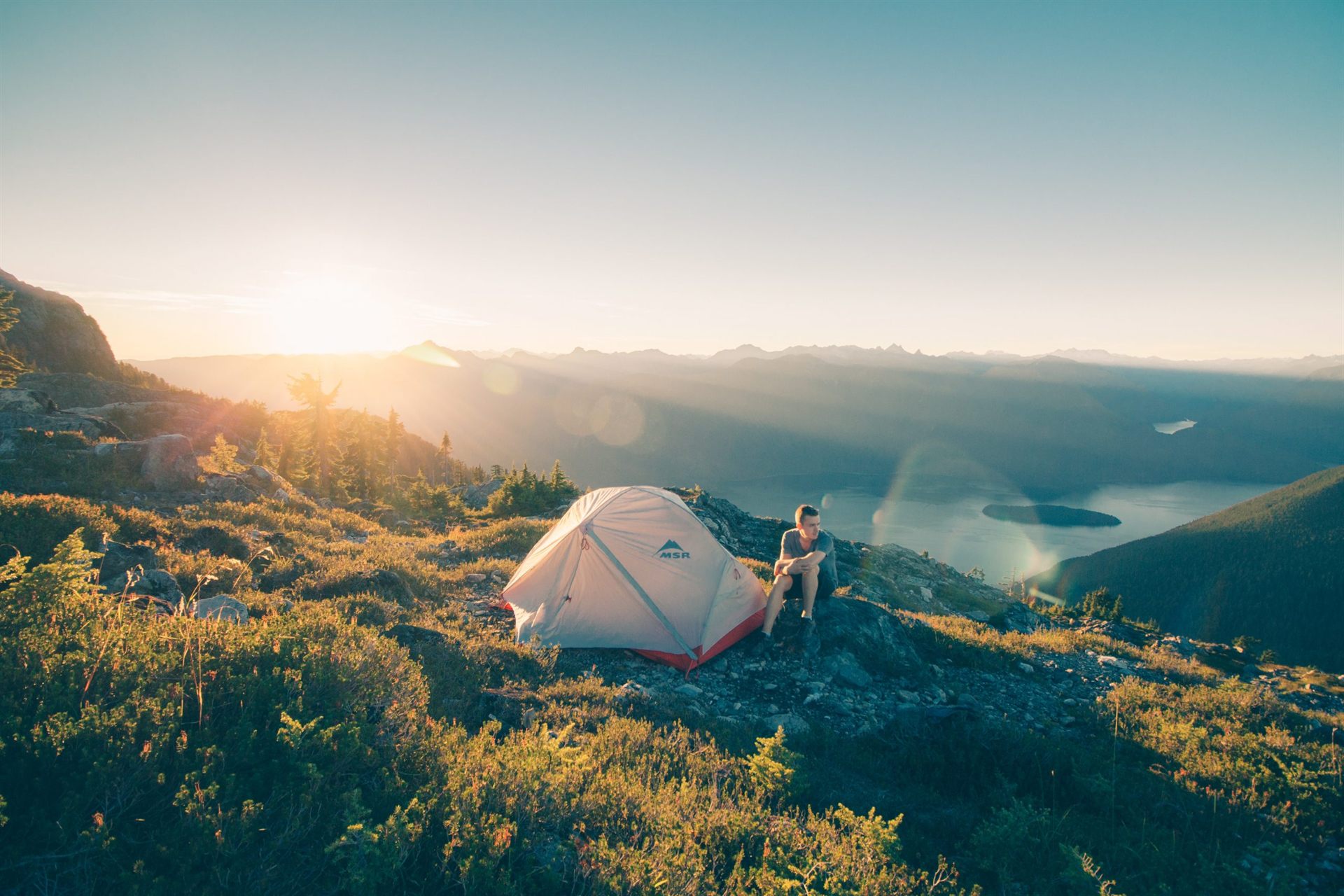 man sitting on stone beside white camping tent