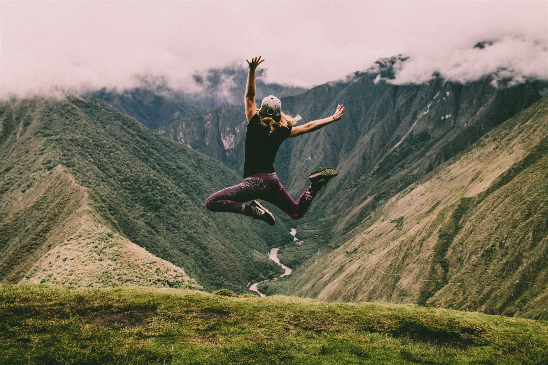 hiker jumping on green mountains