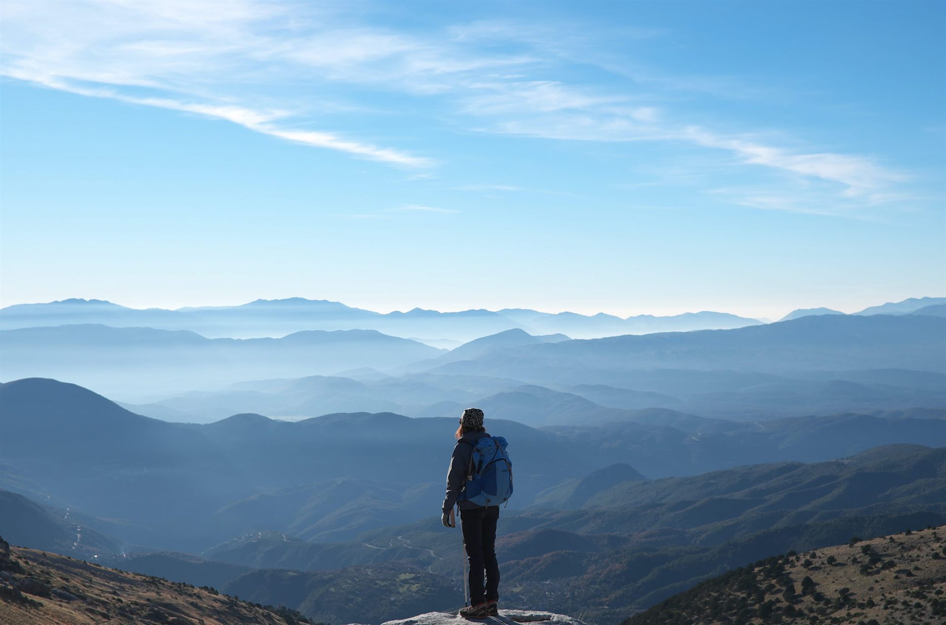 ultralight backpacker wearing backpack standing on cliff in front of mountains during daytime